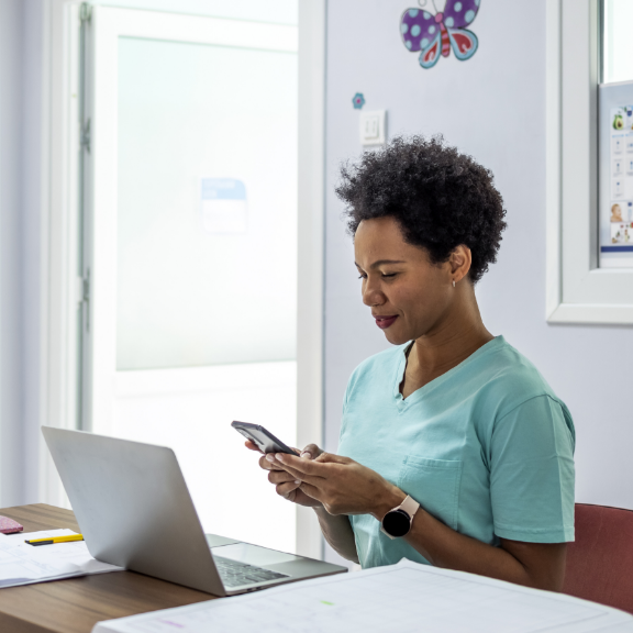 woman behind a laptop looking at something on her smartphone